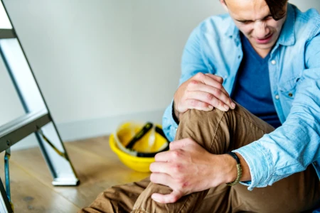 Hombre doliéndose de una rodilla después de caer de una escalera.